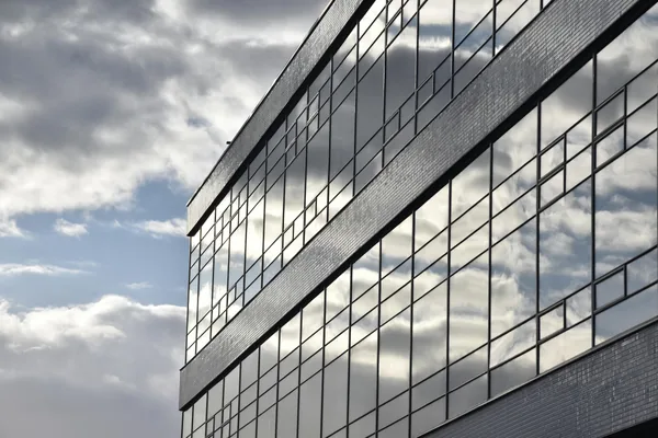 Modern office building facade with reflective glass windows and cloud reflections