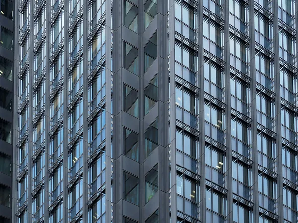 Modern high-rise building facade with repetitive rows of glass windows and metal framework