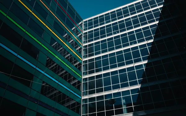 Modern glass office buildings with geometric window grid patterns and colored accent lines