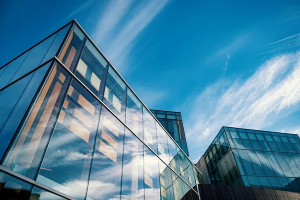 Modern glass building facade reflecting blue sky and clouds above