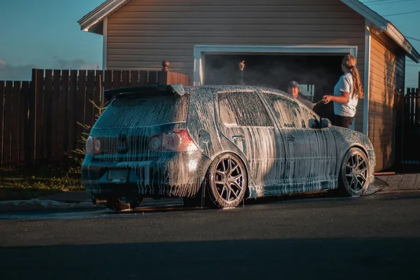 People washing car with water spray in residential driveway setting