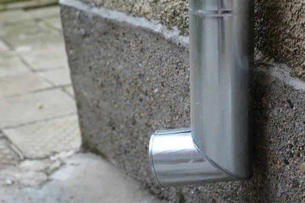 Metal downspout elbow attached to concrete foundation wall outdoors