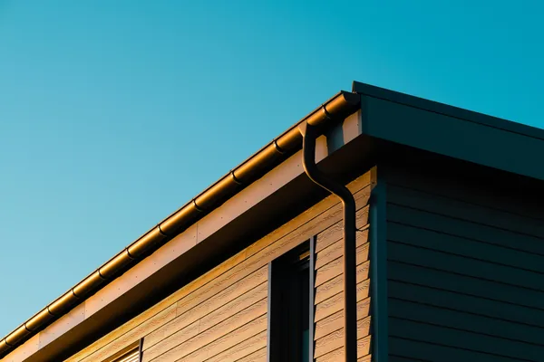 Modern building exterior with metal gutters and downspout against clear blue sky