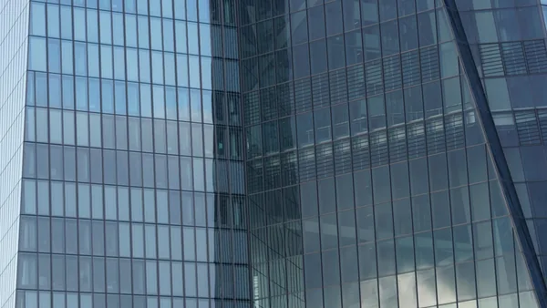 Modern glass building facade with gridded windows reflecting sky and clouds