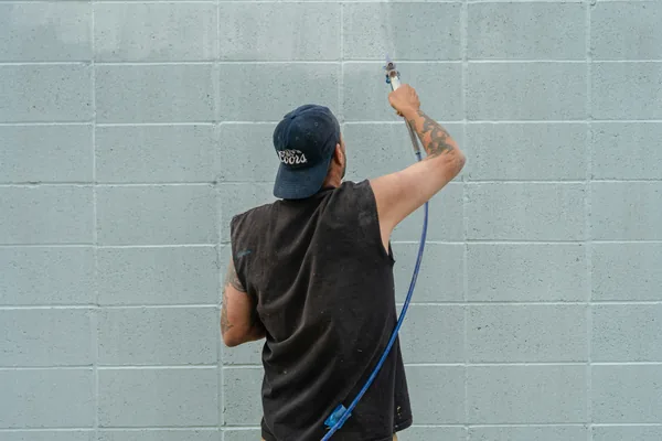 worker cleaning concrete block wall with pressure washer and hose