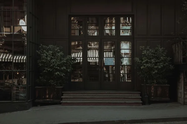 Dark storefront with large glass doors and windows, potted plants flanking entrance